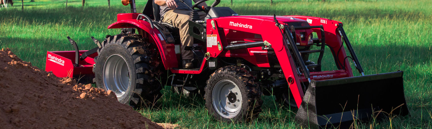 A red Mahindra® tractor moving dirt on a lawn.